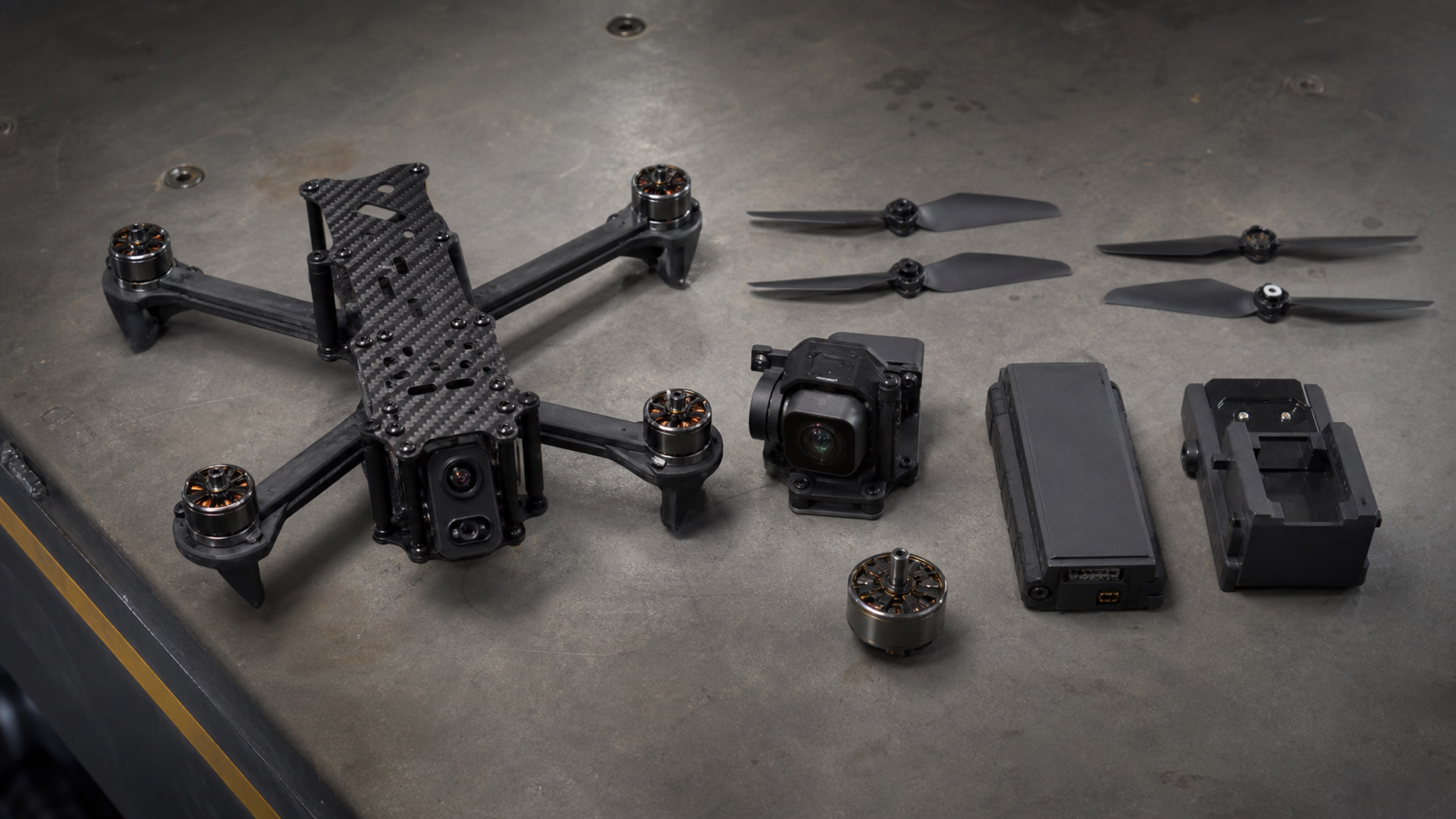 Editorial photo of commercial drone components, propellers, batteries, and thermal camera hardware on an industrial workbench.